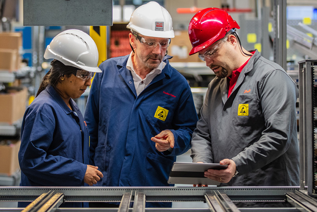 DrivePro partner holding an iPad and explaining something to 2 customers in a factory
