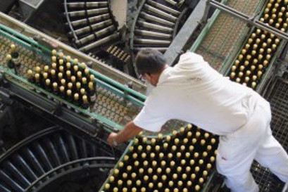 Mitarbeiter beugt sich in einer Abfüllanlage über ein Transportband