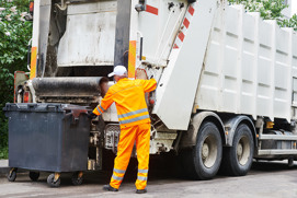 A garbage truck starring a garbage man dressed in all yellow loading a dumpster to be disposed representing compaction pressure control solutions by Danfoss