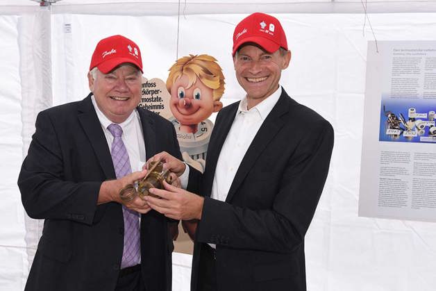 Bestyrelsesformand Jørgen Mads Clausen og CEO Kim Fausing holder den originale termostat, der blev opfundet i 1943 af Mads Clausen, grundlæggeren af Danfoss.